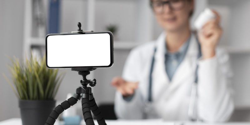 Médica usando celular e computador em atendimento digital na clínica
